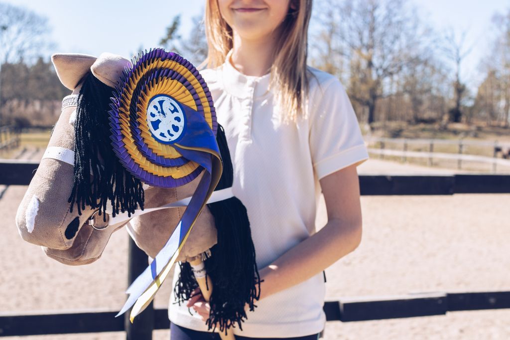 Flicka med käpphäst utanför ridbana.