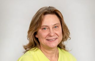 Catarina Eliasson, veterinär på Agria, i Gul veterinär tunika, tittar in i kameran med ett leende.