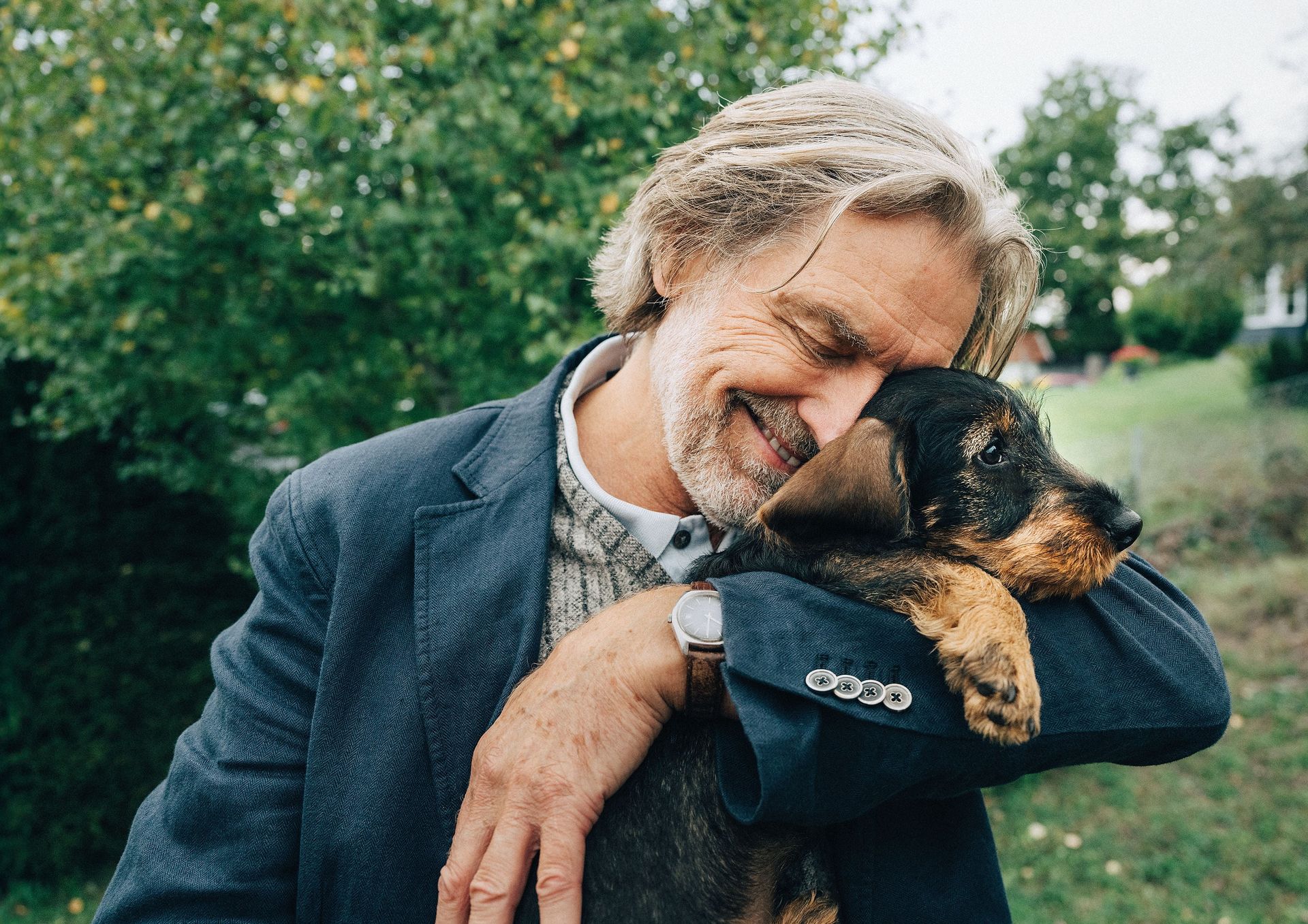 Man kramar om sin hund ute bland grönskande buskar och träd.