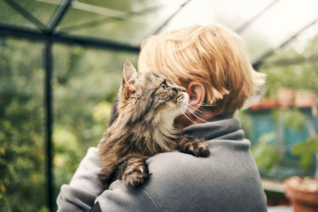 Kvinna som håller katt i växthus.