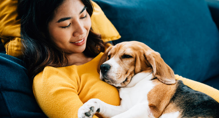 Kvinna som gosar med sin hund i soffan, ett exempel på trygghet och närhet i hundens beteende.