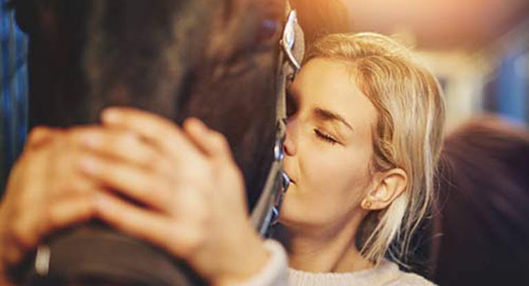 Kvinna gosar med häst i stallet.