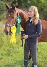 Ponnyn Lizzie med två tävlingsrosetter bredvid sin matte.