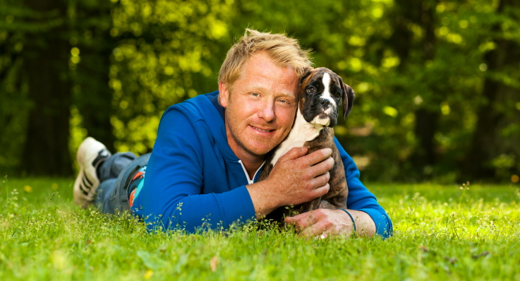 Fredrik Steen ligger i gräset och myser med en boxervalp.